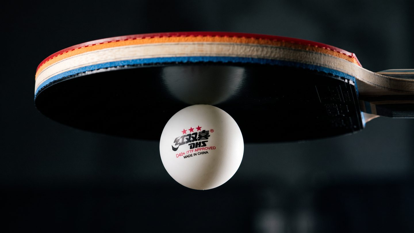 A table tennis ball held motionless against the tacky surface of an inverted rubber on a racket.